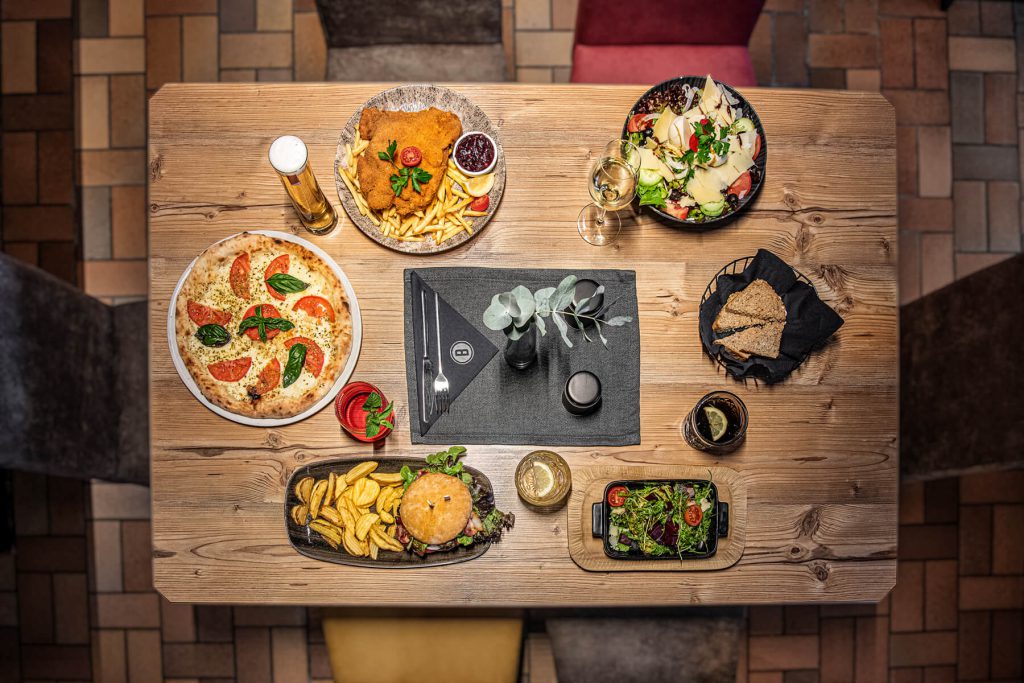 Holzofenpizza, Schnitzel, Burger und Salat auf Holztisch im Restaurant Bad Hofgastein